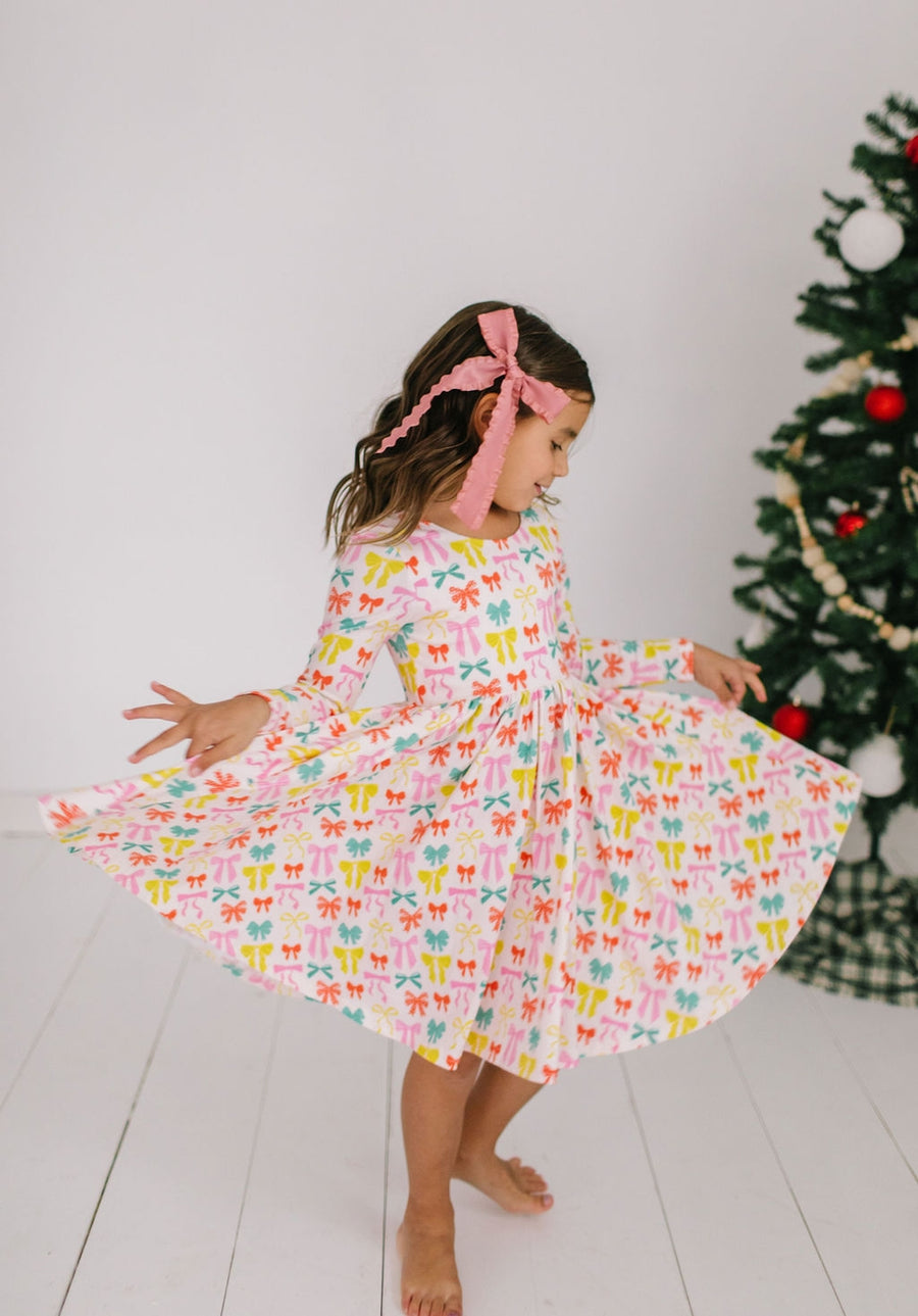 Child in a colorful dress brightly colored bows on it with a Christmas tree in the background