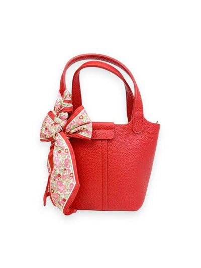 red satchel with two handles and pink and red floral scarf tied to the handles. 