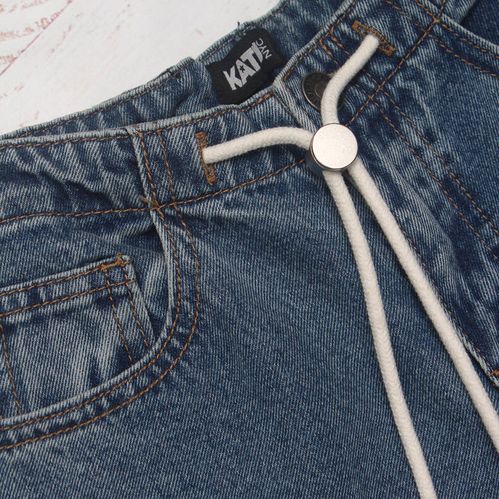 Close-up of blue jeans with a white lace detail and 'KATIE' label.