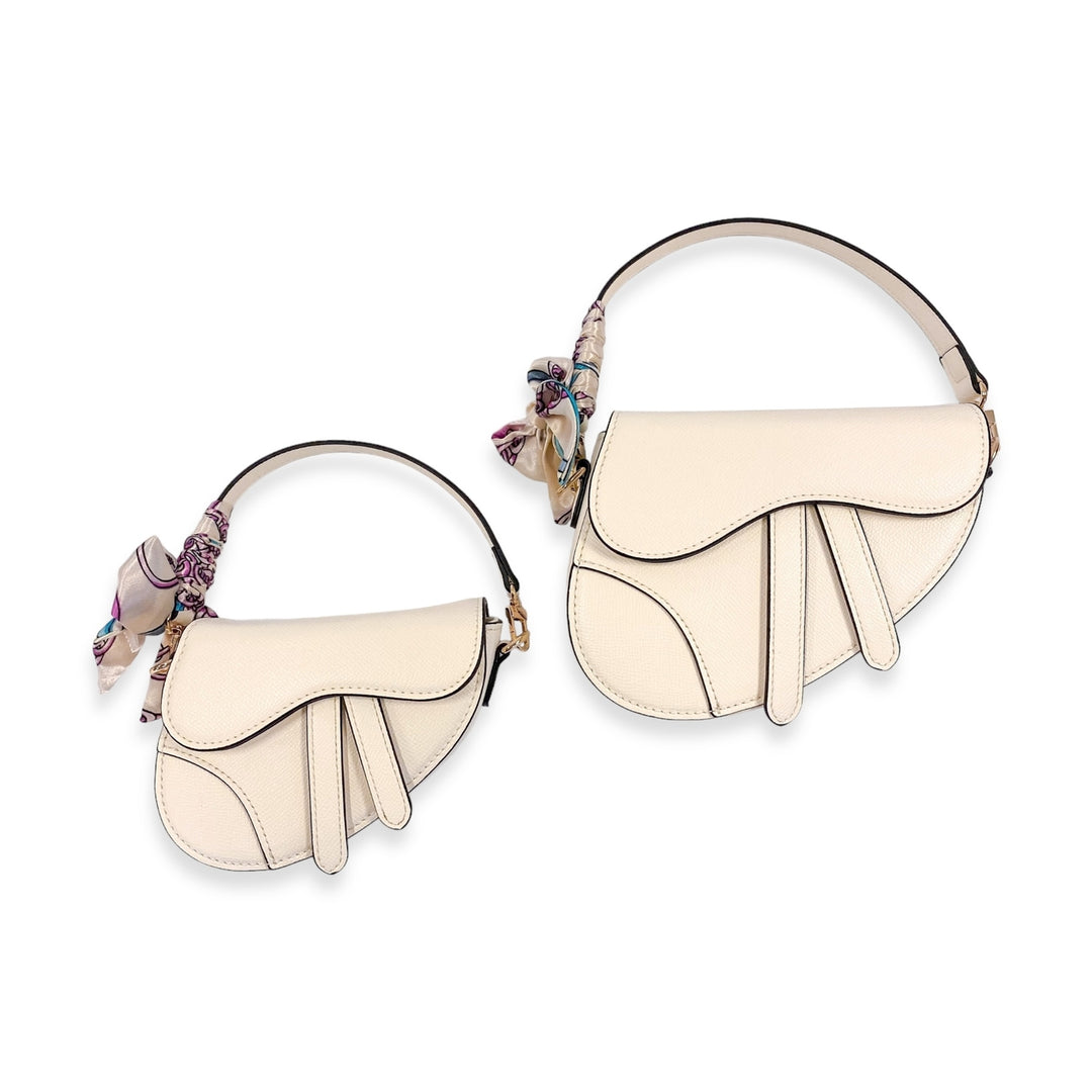 Two cream-colored saddle handbags with floral accents on a white background