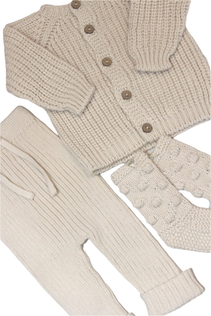 knit baby items in creme color: cardigan sweater, knit pants, and baby booties. 