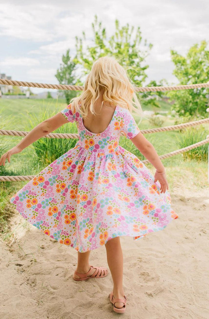 young girl twirling around in the vibrant floral dress, this shows the back of the dress with a ballet back and full skirt. 