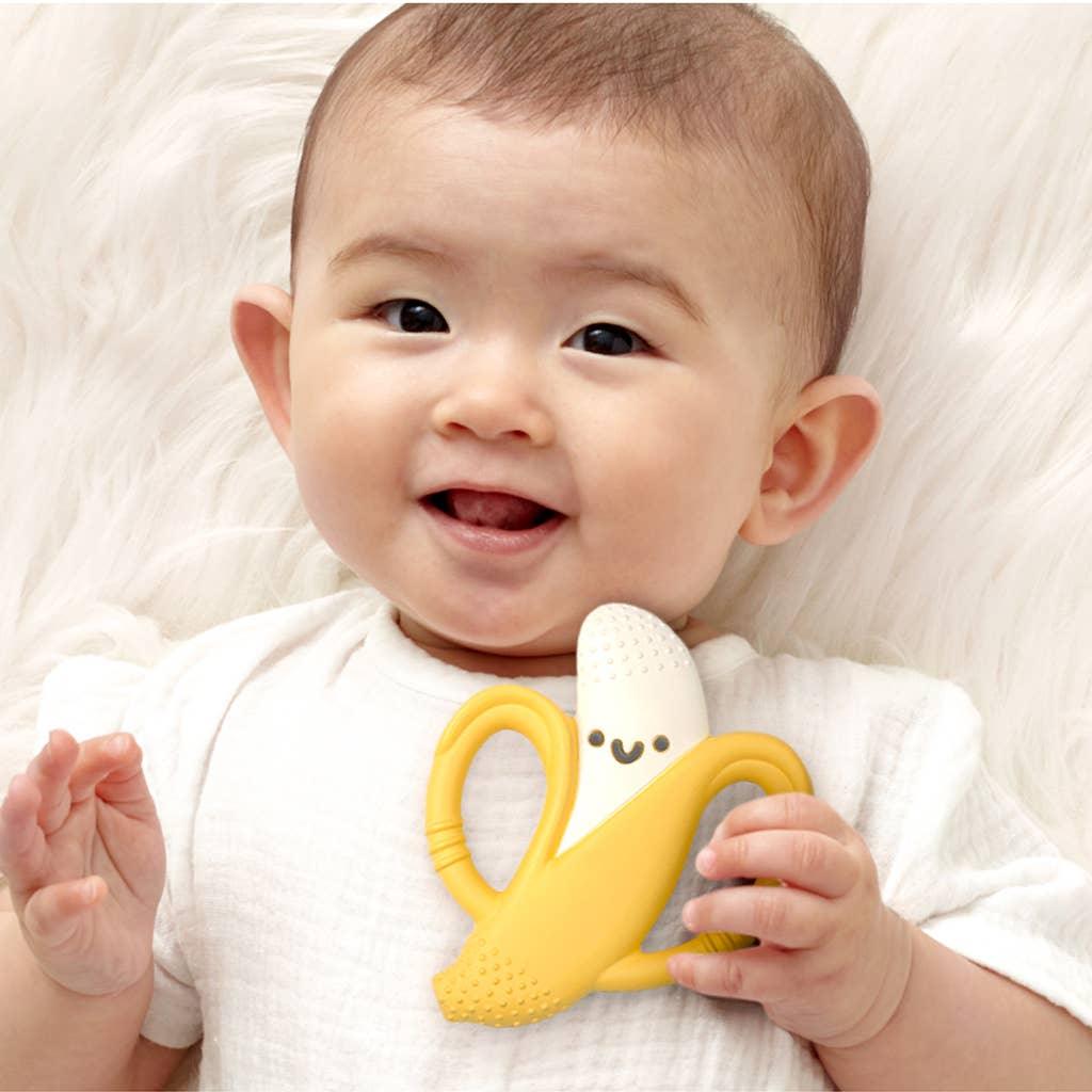 baby posing with banana chew toy, holding onto the banana teether on one of the handles. 