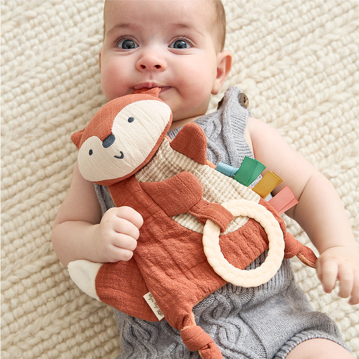 Baby holding a soft toy with a textured surface on a beige blanket