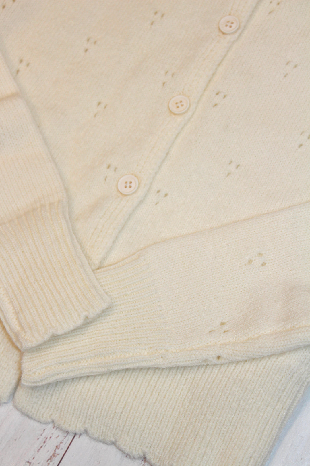 Close-up of a creamy yellow-colored cardigan with button details on a wooden surface