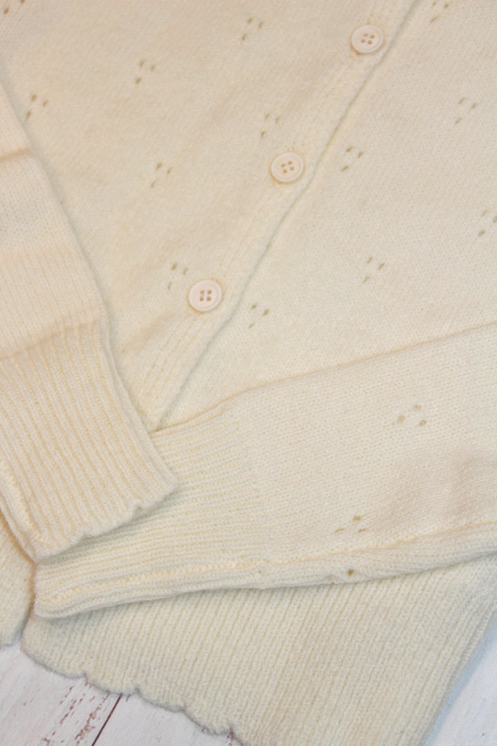 Close-up of a creamy yellow-colored cardigan with button details on a wooden surface