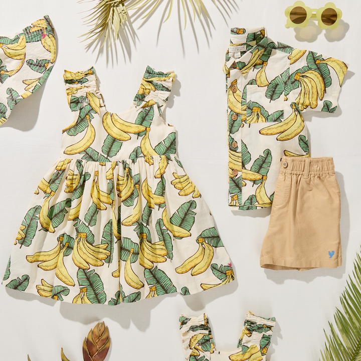 Children's clothing set with banana print dress, shorts, and accessories on a white background.