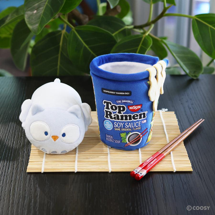 plush owl sitting next to a ramen cup in Soy Sauce flavor that the owl would fit inside. 