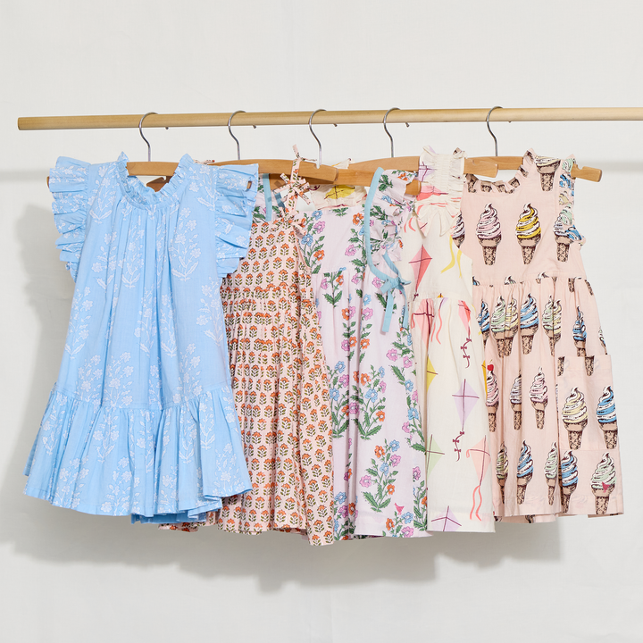Five children's dresses with different patterns hanging on a rack against a white background