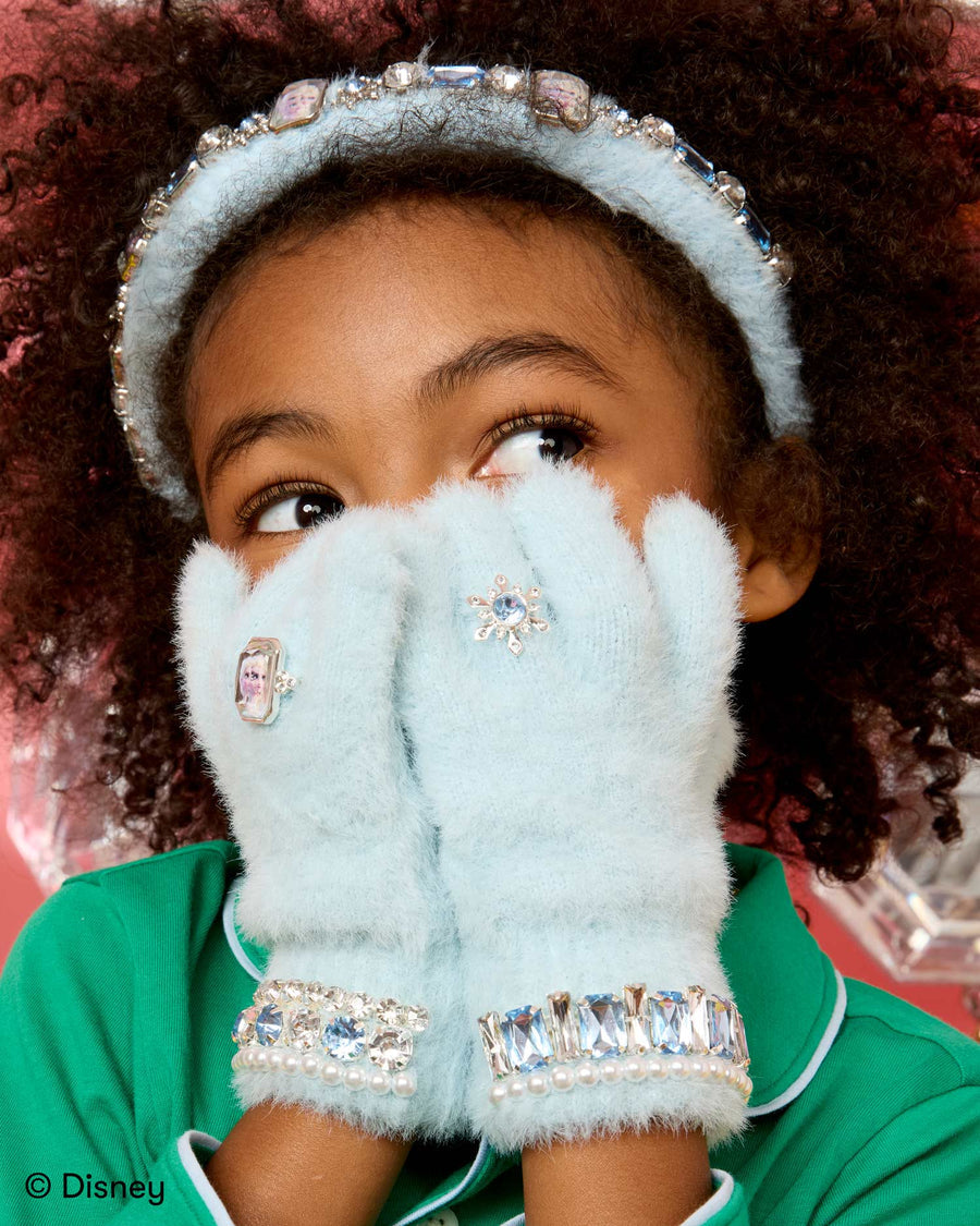 Child wearing light blue gloves with rhinestone accents and a Disney shirt, against a red background.