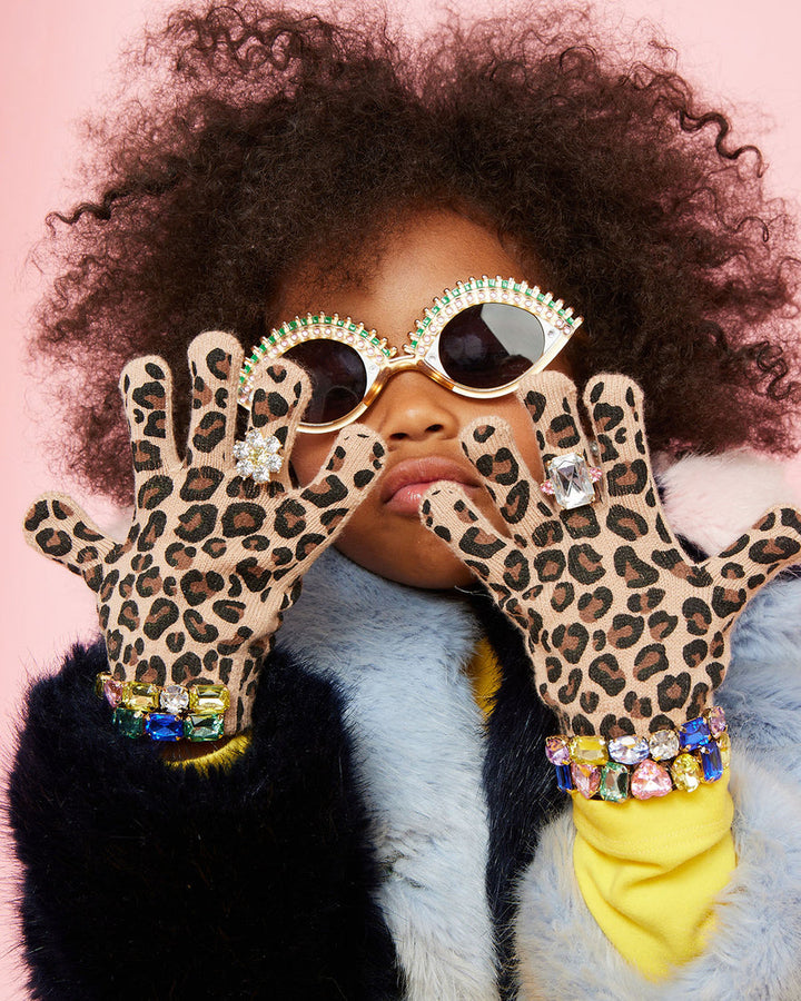 Child wearing leopard print gloves with rhinestones and sunglasses against a pink background