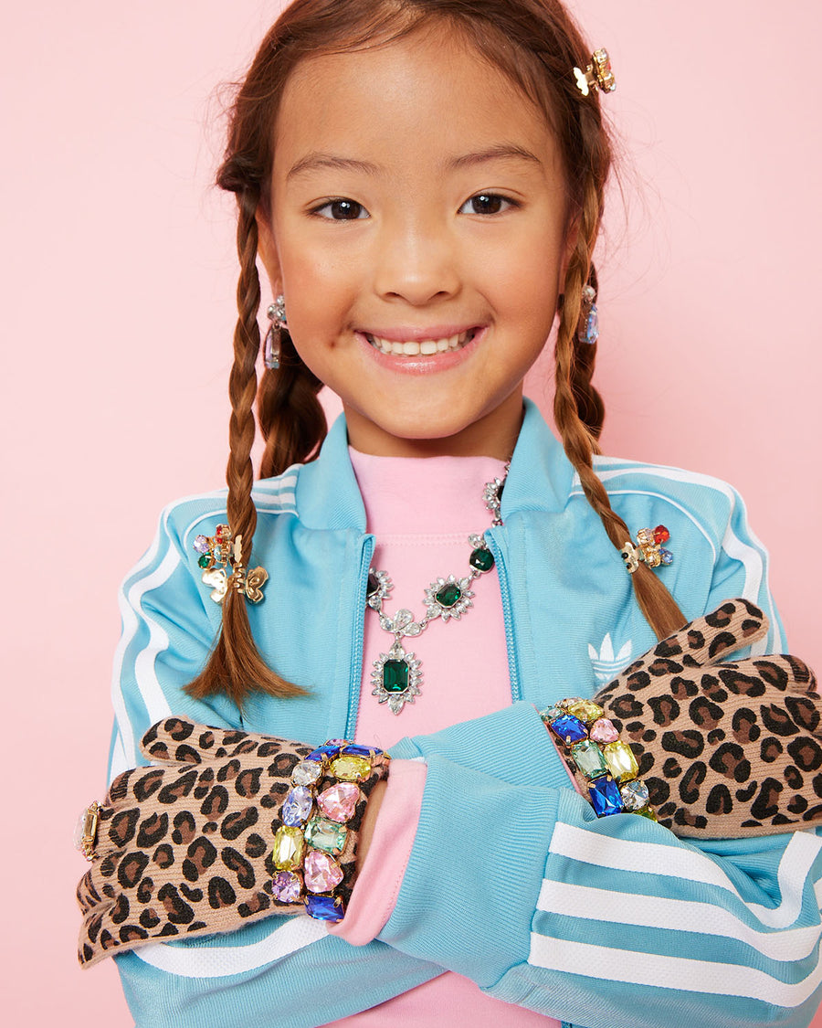 Young girl wearing a blue jacket with gemstones and leopard print gloves on a pink background