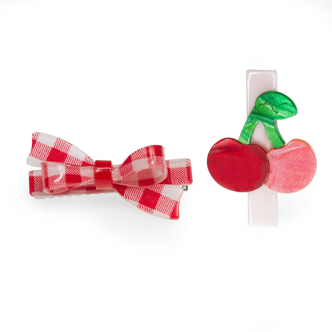 Two hair clips, one with a red checkered bow and the other with a cherry design, on a white background.