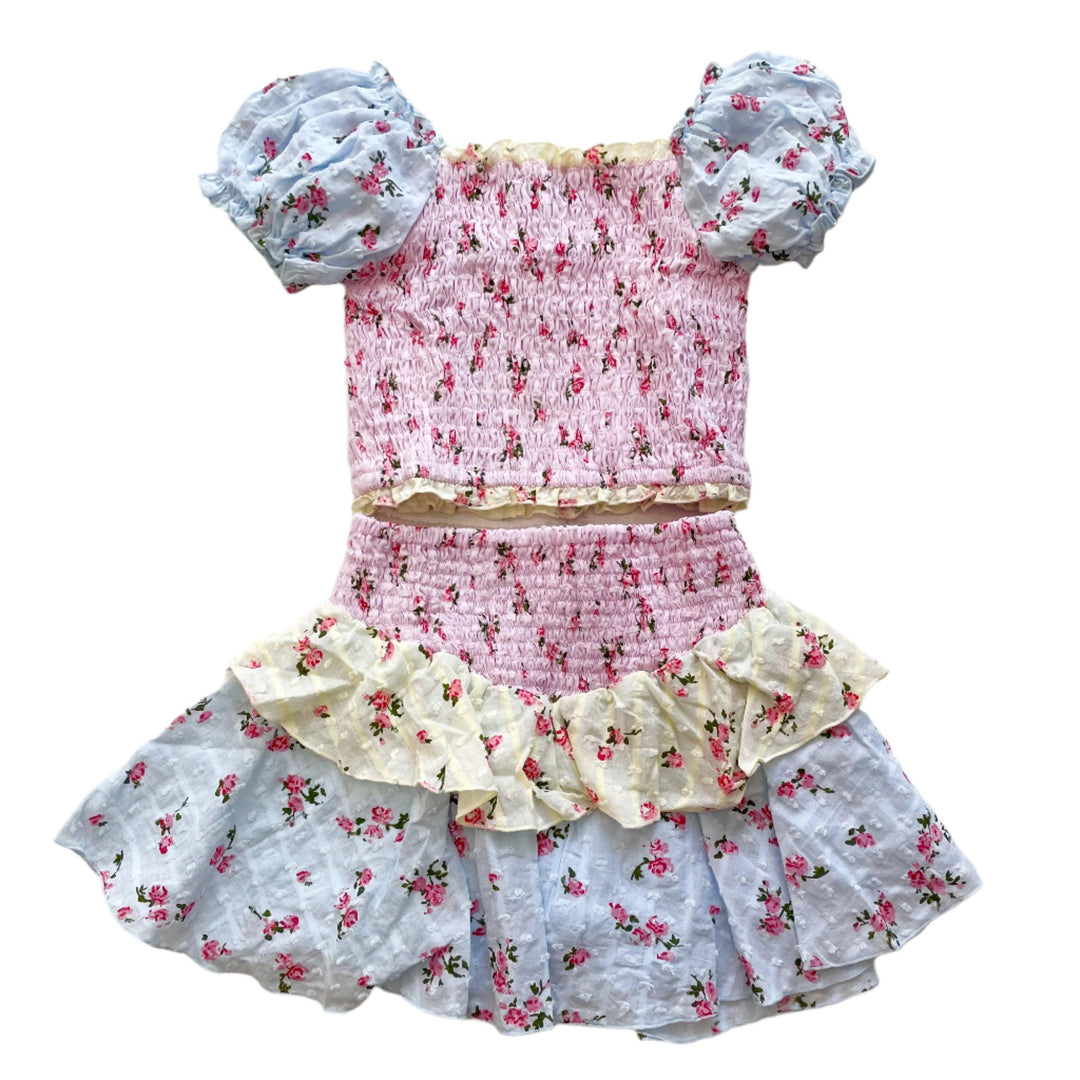 smocked top with puff sleeves and skirt with smocked top and 2 ruffles at the bottom. each layer of fabric has a different color: blue, yellow and pink. sleeves are blue. body is pink and first skirt ruffle is yellow. last skirt ruffle is blue