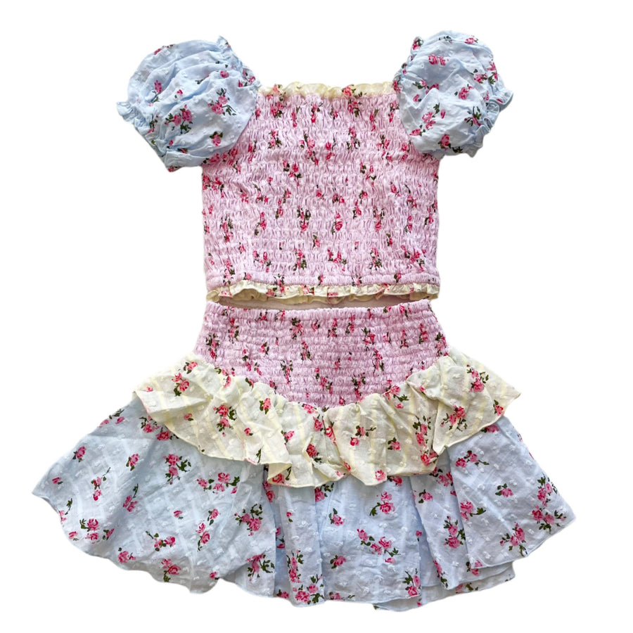 smocked top with puff sleeves and skirt with smocked top and 2 ruffles at the bottom. each layer of fabric has a different color: blue, yellow and pink. sleeves are blue. body is pink and first skirt ruffle is yellow. last skirt ruffle is blue