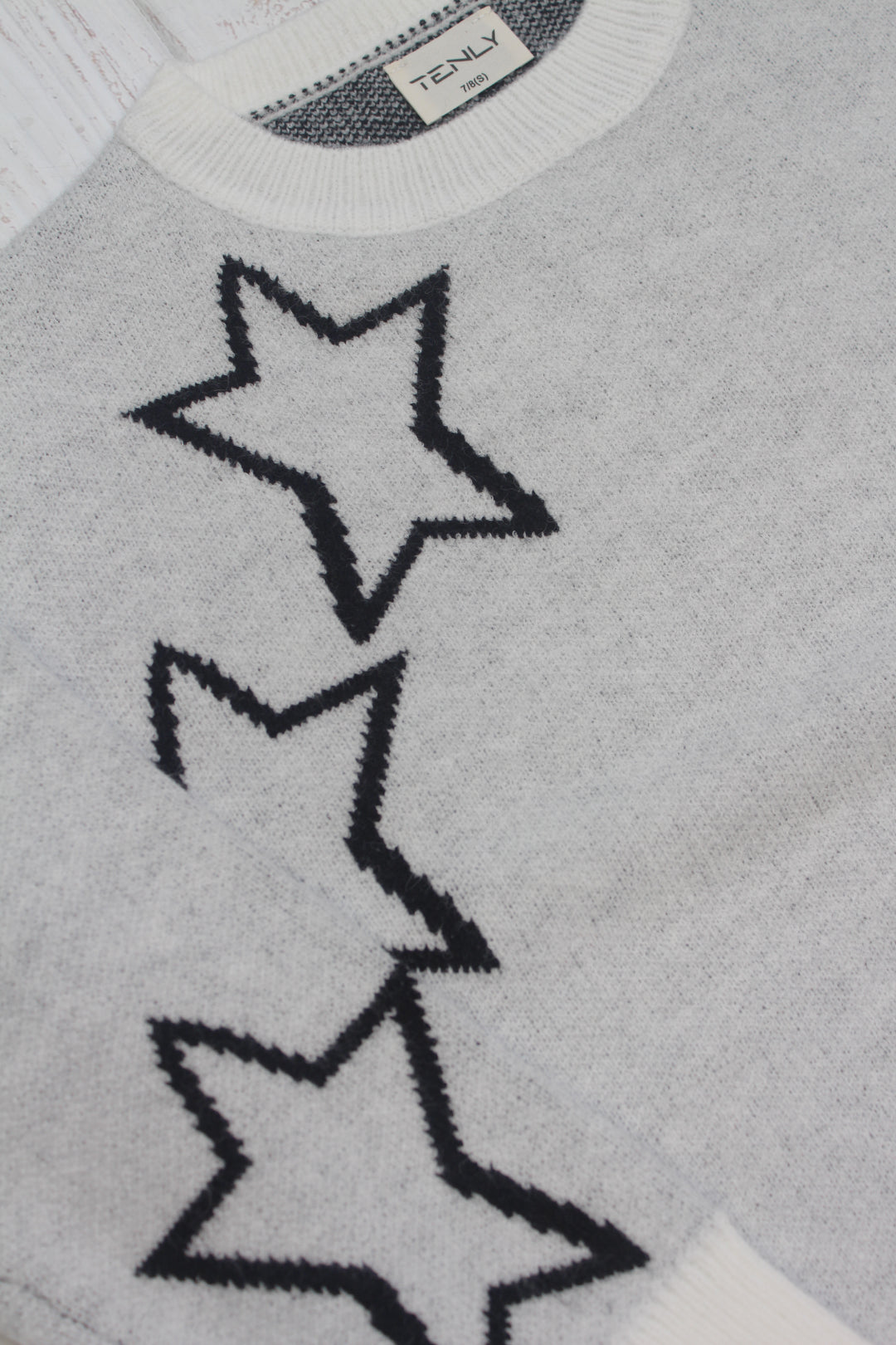 Gray sweater with star patterns and a brand label on a gray background