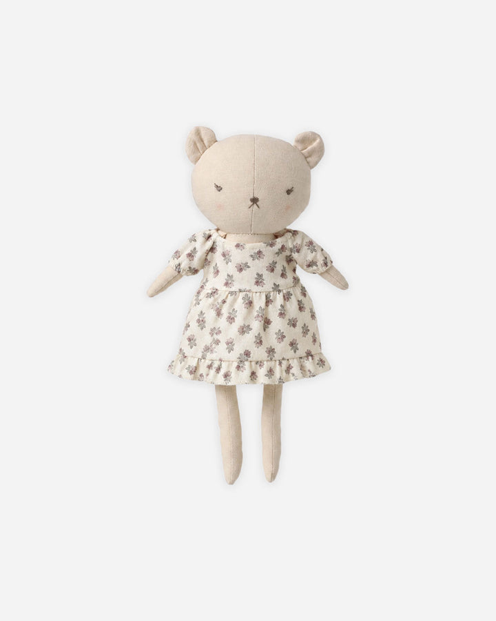 A plush teddy bear doll with a cream-colored fabric body, wearing a matching cream dress with a small brown floral pattern, set against a solid light gray background.