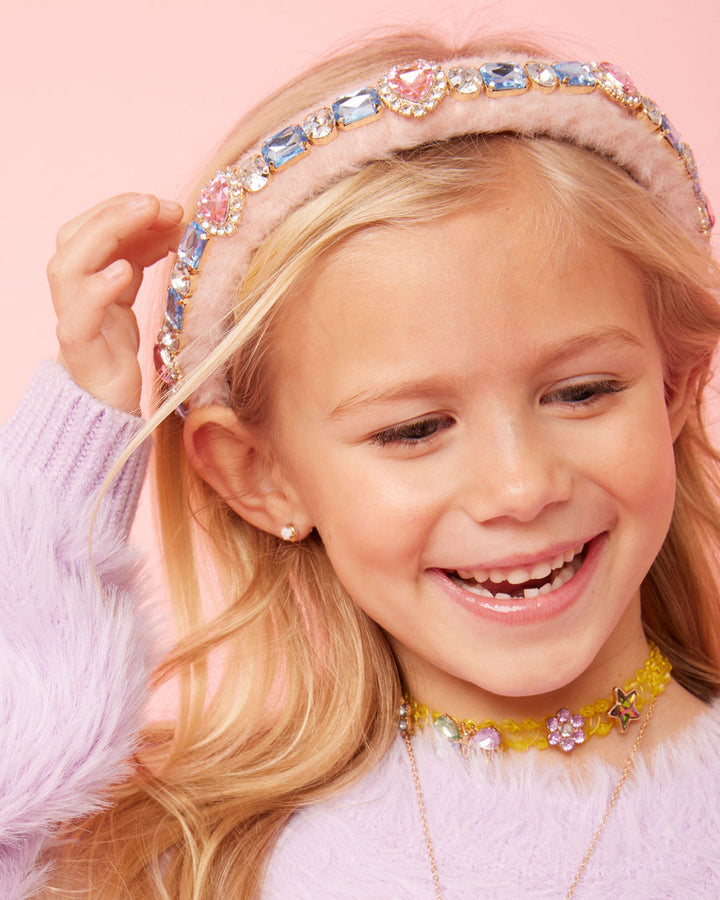 Young girl wearing a colorful headband and necklaces against a pink background