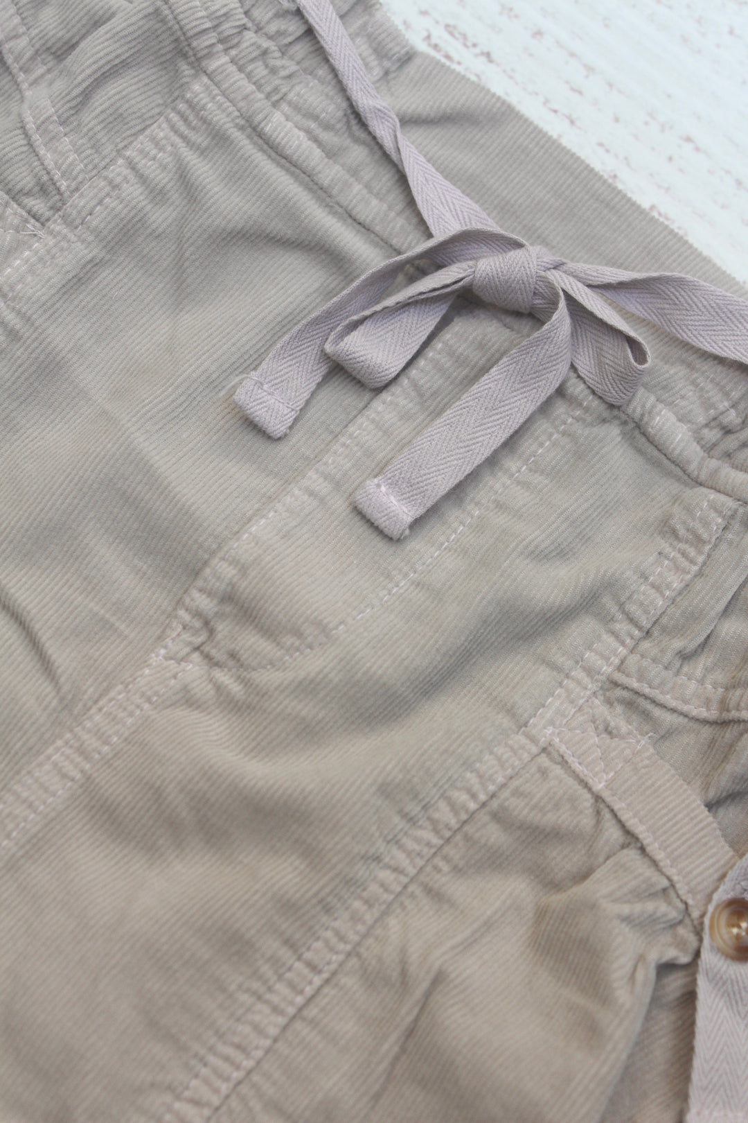 Close-up of beige shorts with a tie and button details.