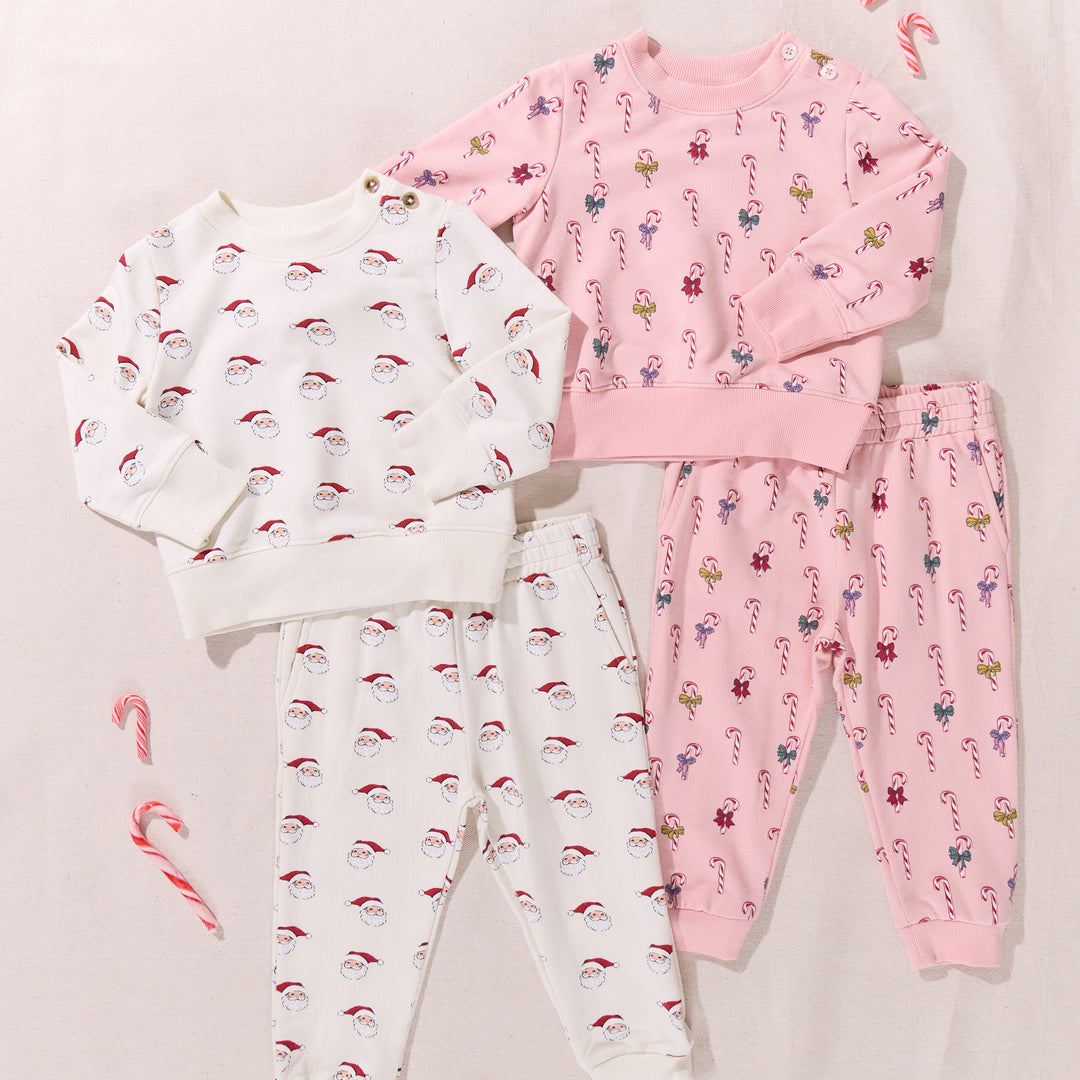 Two children's pajama sets, one white with red hats and the other pink with candy cane patterns, on a light background.