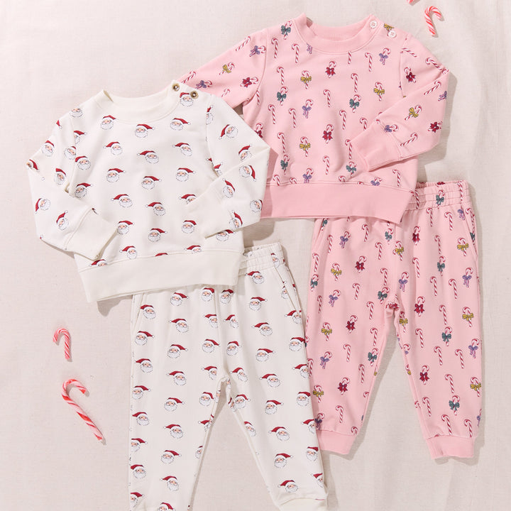 Two children's pajama sets, one white with red hats and the other pink with candy cane patterns, on a light background.