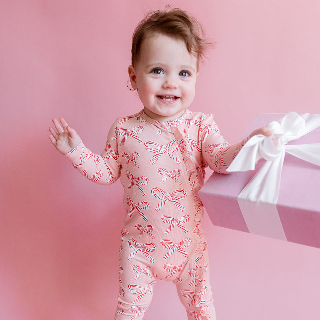 Child wearing a pink onesie with candy cane pattern on a pink background