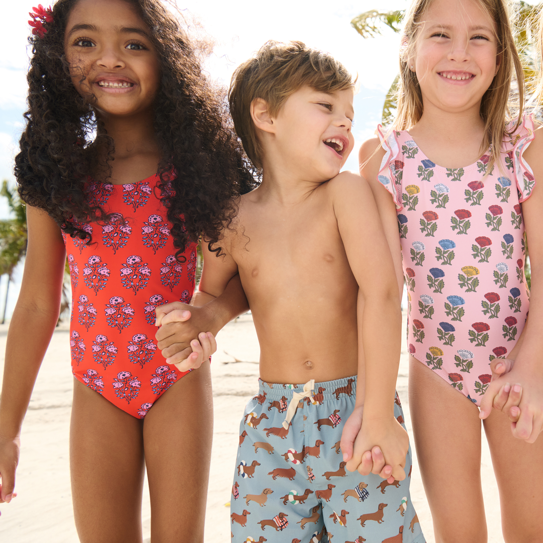 Three children in swimsuits standing together on a beach.