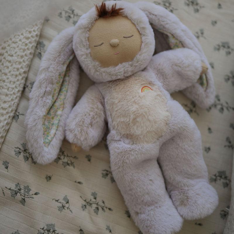 doll dressed up as a bunny and laying on ythe floral bedding. 