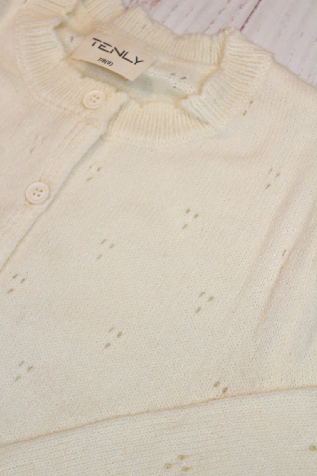 Close-up of a cream-colored cardigan with a brand label on a light wooden surface.