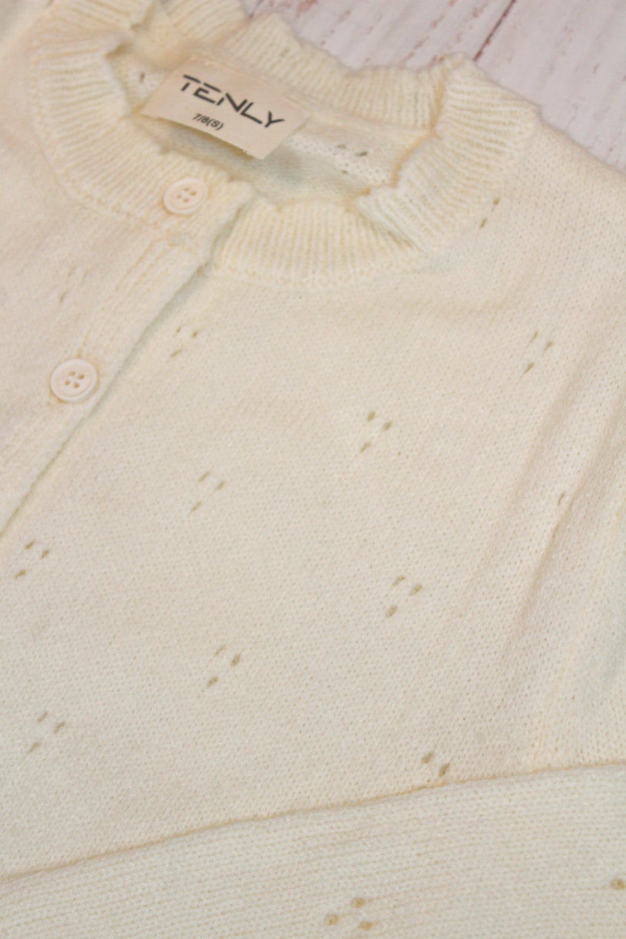 Close-up of a cream-colored cardigan with a brand label on a light wooden surface.