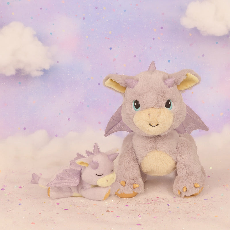 Two dragon-shaped plush toys on a soft, cloud-like surface with a pastel sky background.