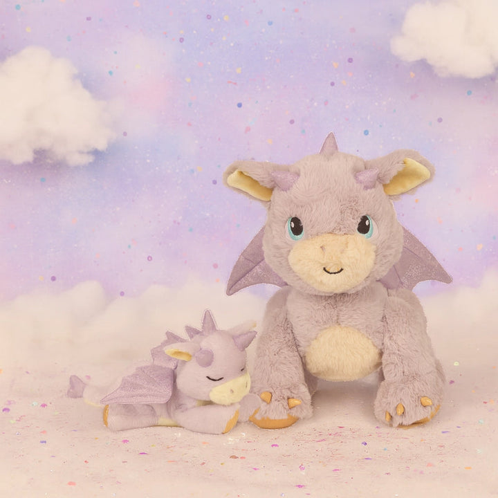 Two dragon-shaped plush toys on a soft, cloud-like surface with a pastel sky background.