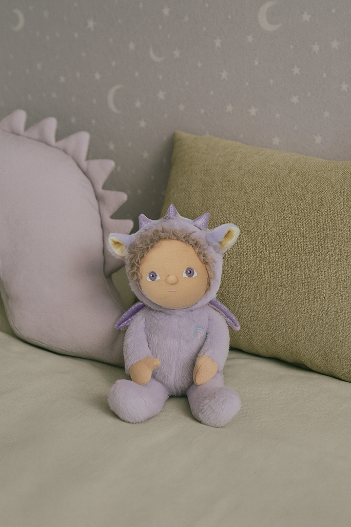 Stuffed animal in a dragon costume sitting on a bed with a star-patterned wall in the background.