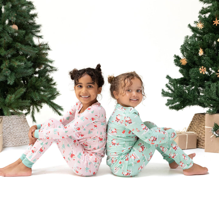 Two children in pajamas sitting on the floor with Christmas trees in the background