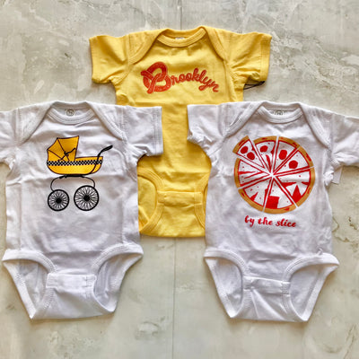 baby onesies all NY themed, one Brooklyn pizza, one Brooklyn pretzel and one NYC baby buggie