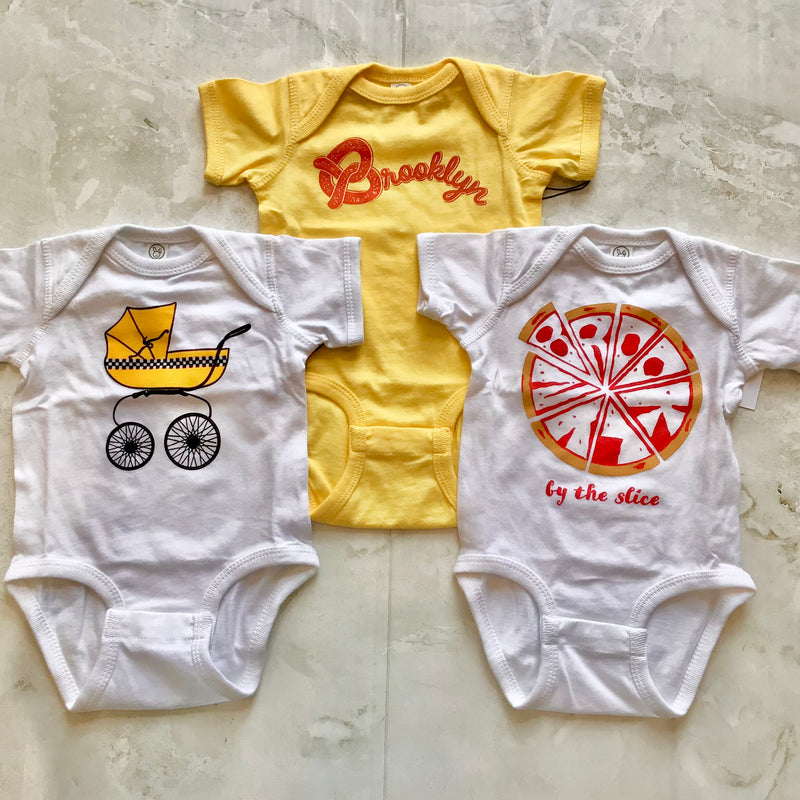 baby onesies all NY themed, one Brooklyn pizza, one Brooklyn pretzel and one NYC baby buggie