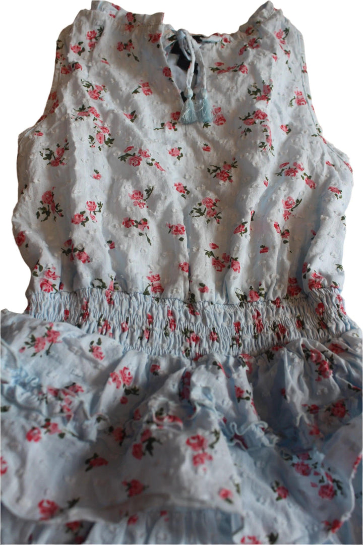 close up of the fabric for the girls dress, light blue with tiny pink roses all over it. it shows you the elastic waist and the ruffles. 