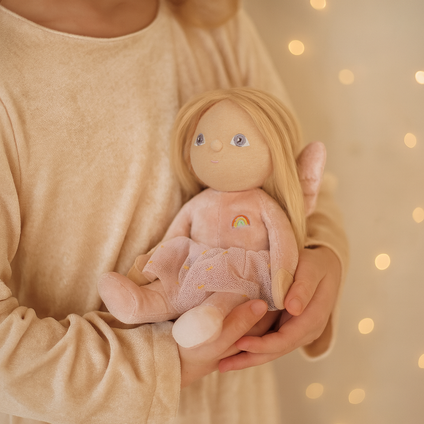 Person holding a small doll with a soft texture against a warm, blurred background
