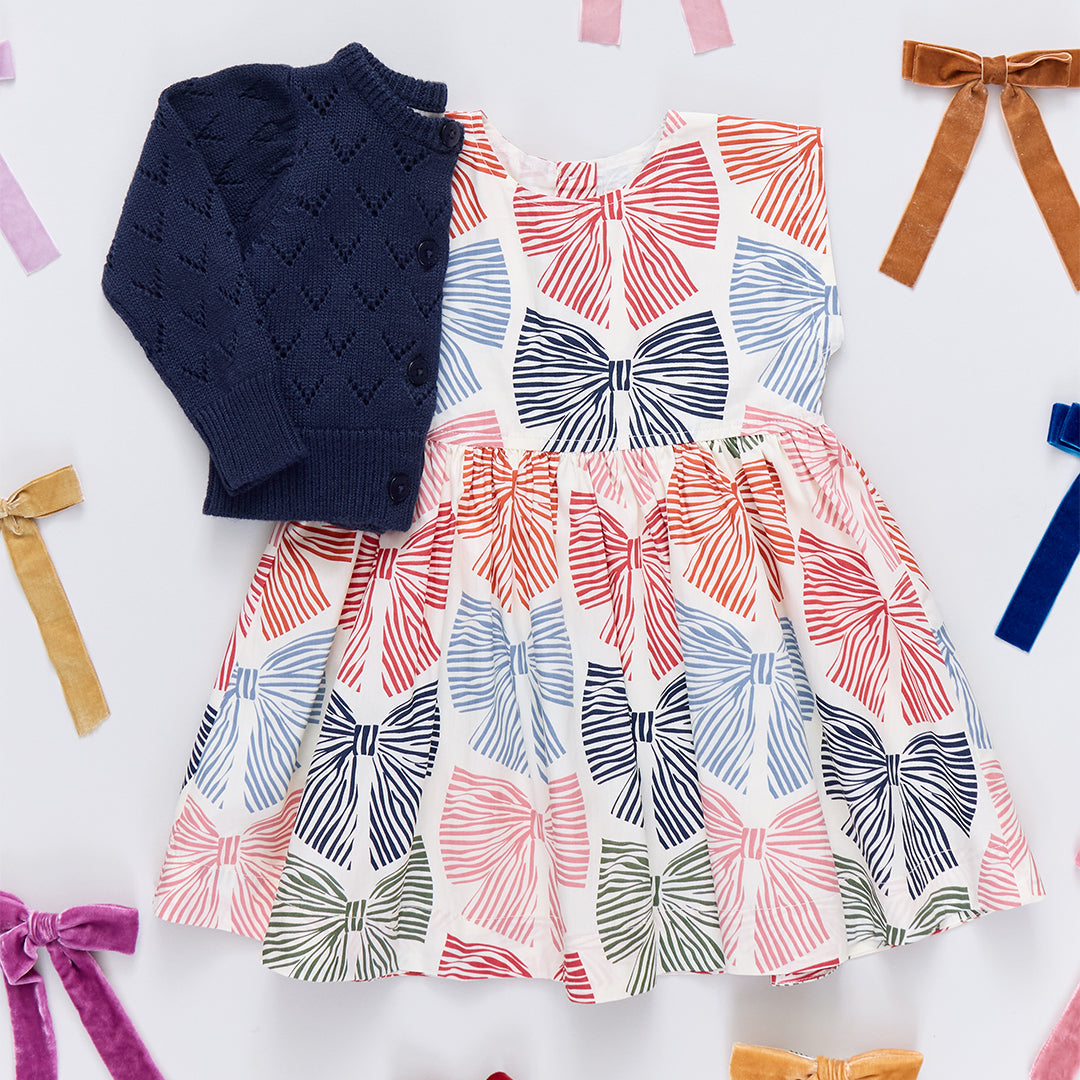 Dress with bow pattern and navy sweater on a white background with colorful ribbons.