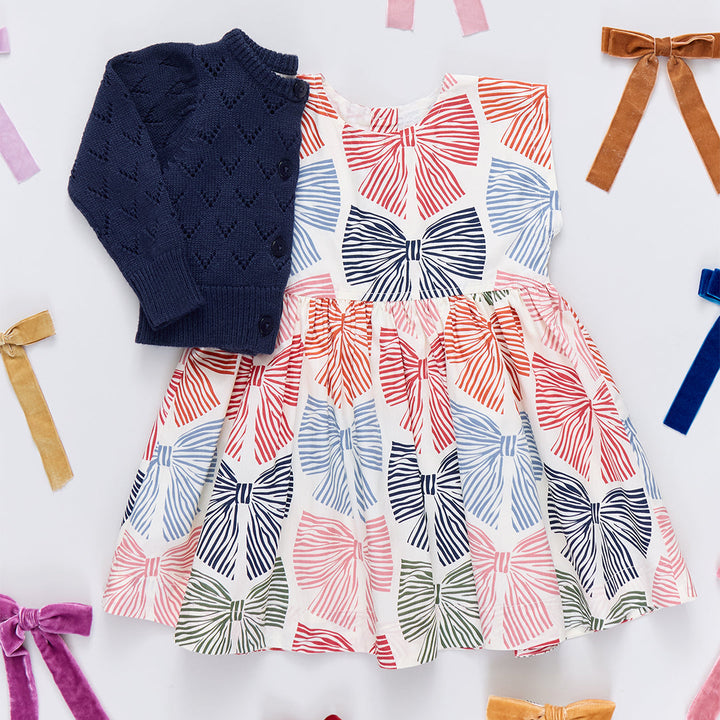 Dress with bow pattern and navy sweater on a white background with colorful ribbons.