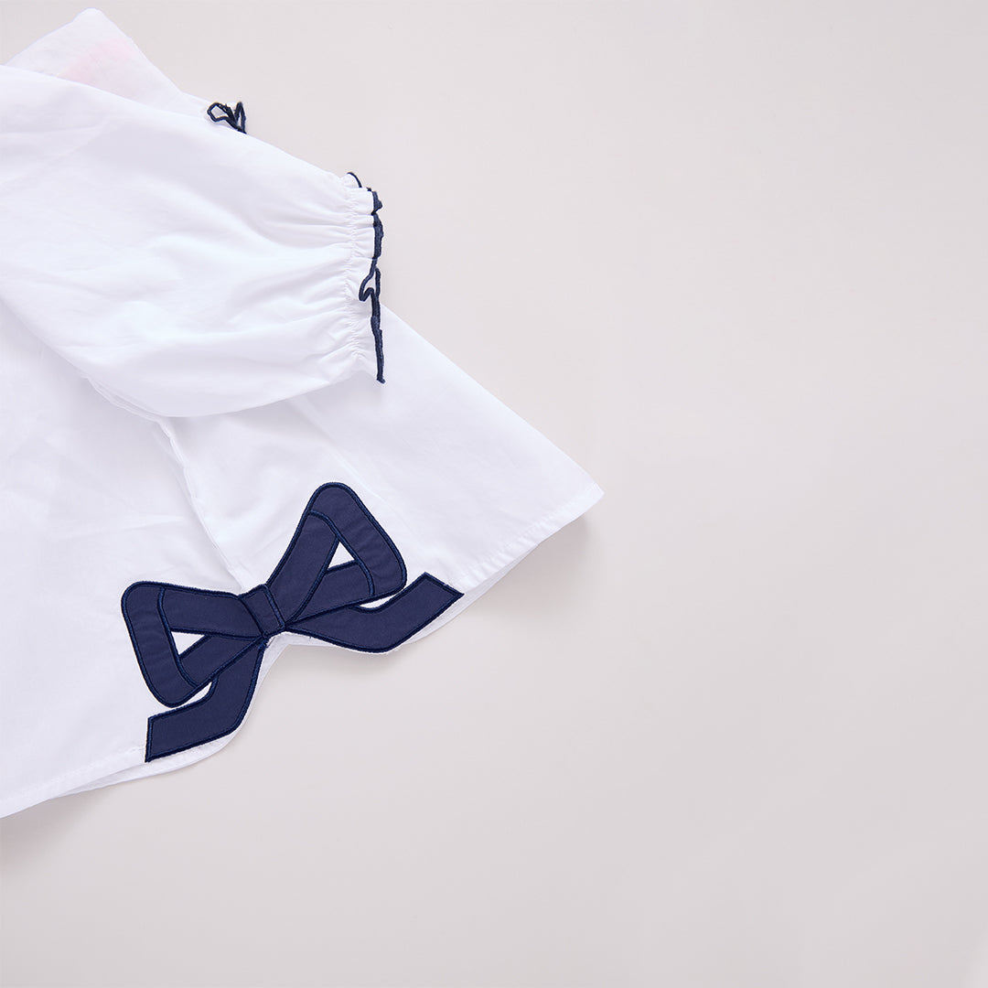 white blouse with navy grosrain bow at the bottom of the shirt