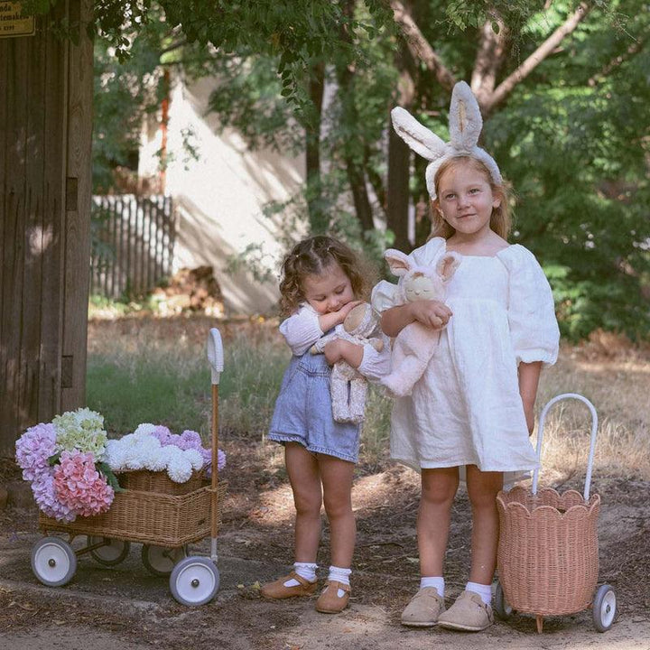 two little girls playing outside and one of them is wearing gray plush bunny ears. 