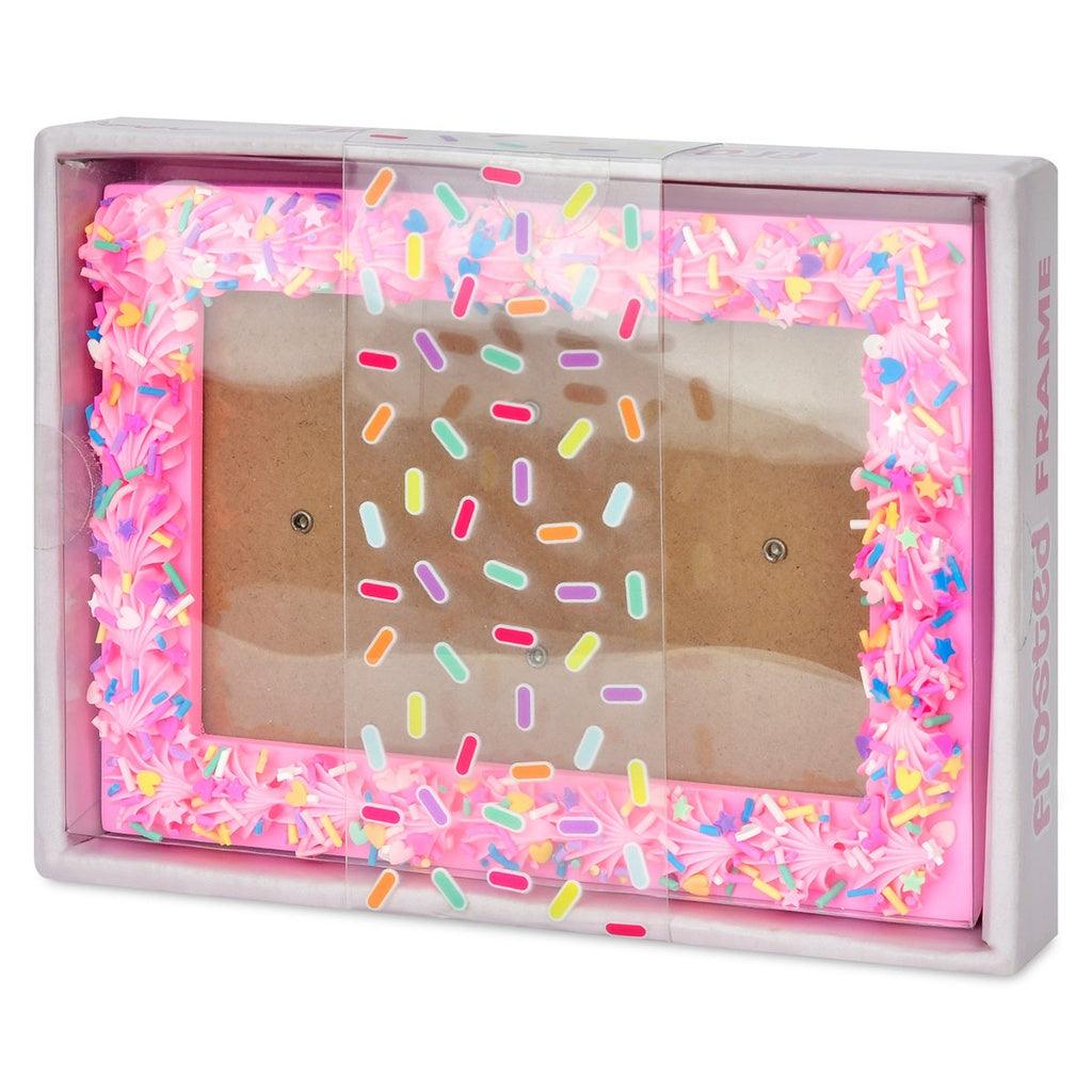 picture frame with pink frosting on the outline of it with rainbow sprinkles on top of the frame. 
