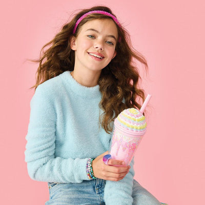 Girl holding a pink tumbler with what looks like frosting piped on top. 