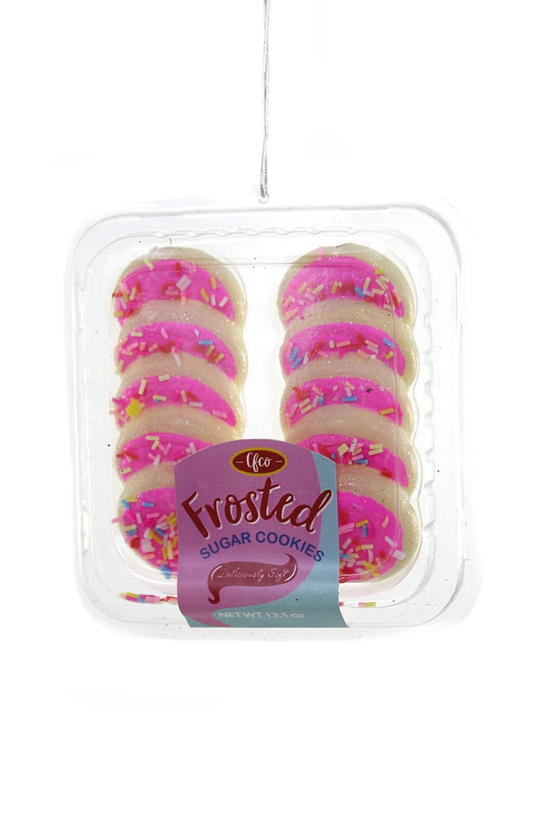 holiday ornament that has sugar cookies frosted in pink icing with sprinkles in a to go plastic container. 