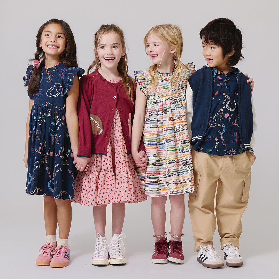 Four children standing together wearing colorful outfits 