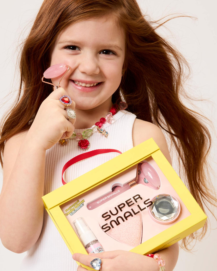 Young girl holding a 'Super Smalls' product box with lip gloss and other items.