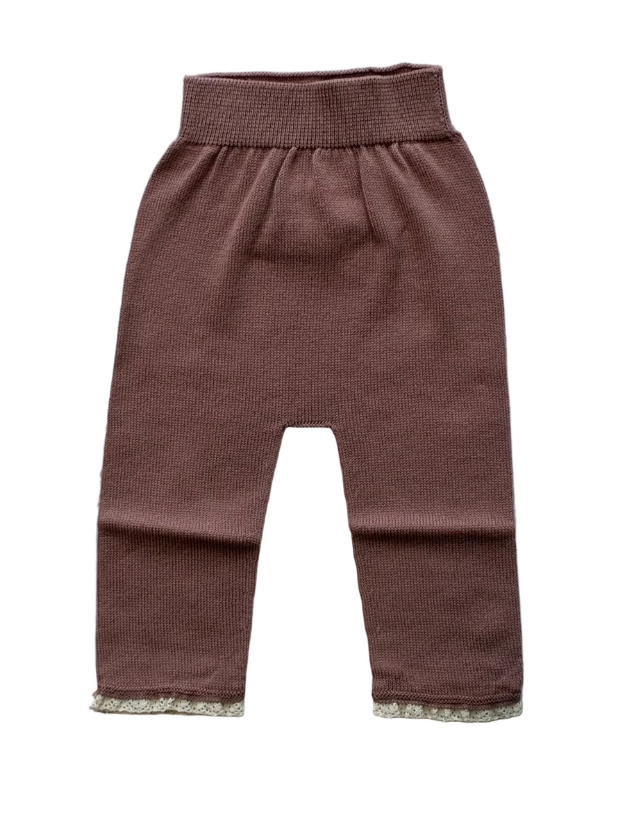 A pair of baby knit pants in a dusty rose-brown color, featuring a wide elastic waistband and delicate lace trim at the ankle cuffs, laid flat on a light gray wood plank background.