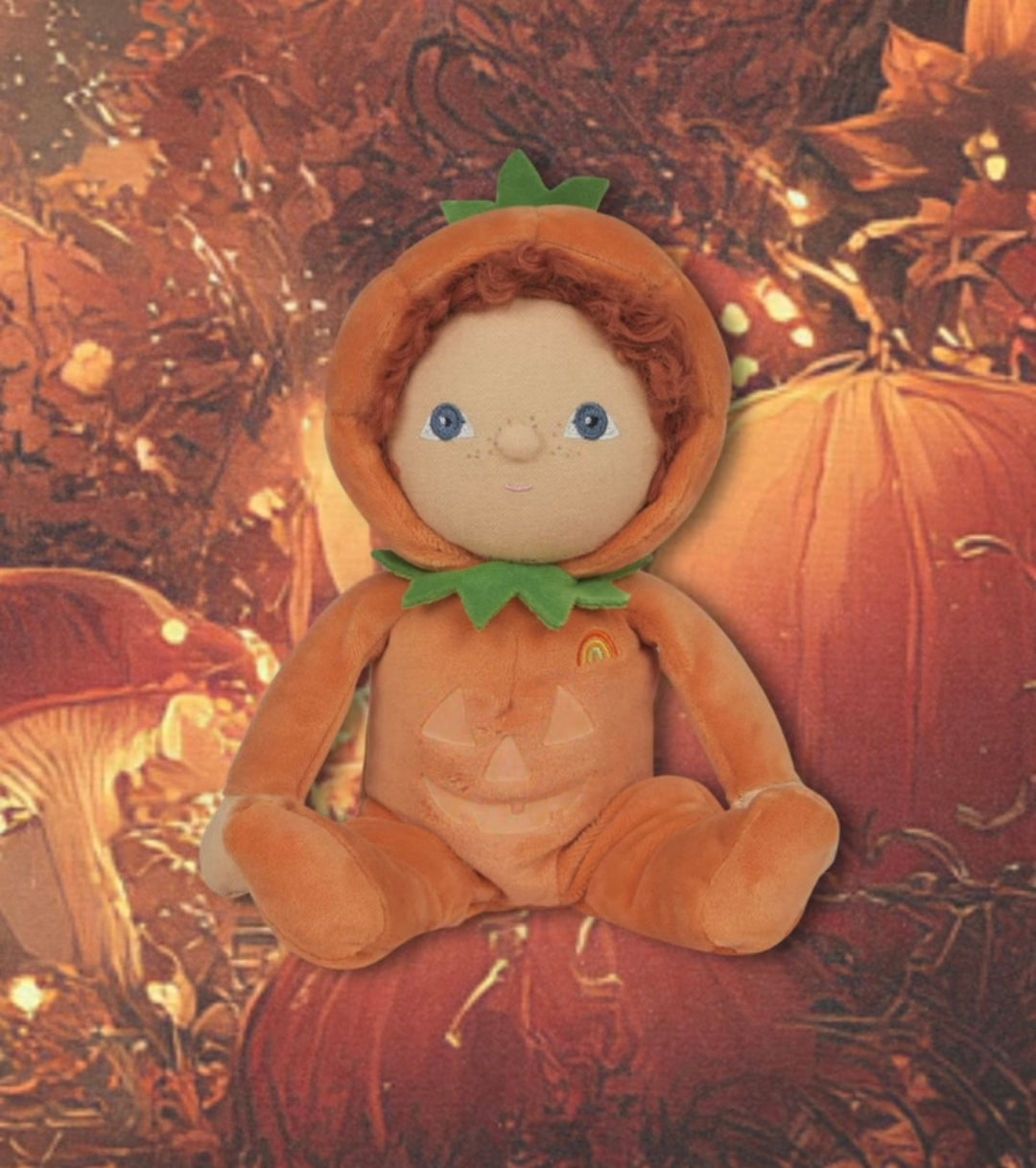 Plush toy dressed as a pumpkin with a textured autumn background