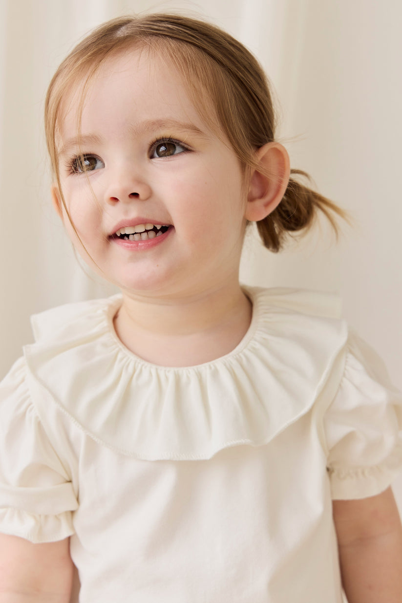 Young girl wearing a white shirt with ruffled collar against a plain background